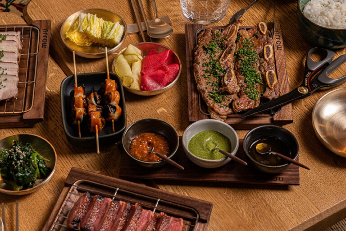Korean-style spread on wooden table at Mojju: grilled meats, skewers, banchan, and dipping sauces