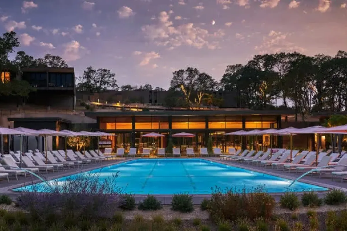 Hotel pool at dusk with lounge chairs and umbrellas, glowing building and trees in background