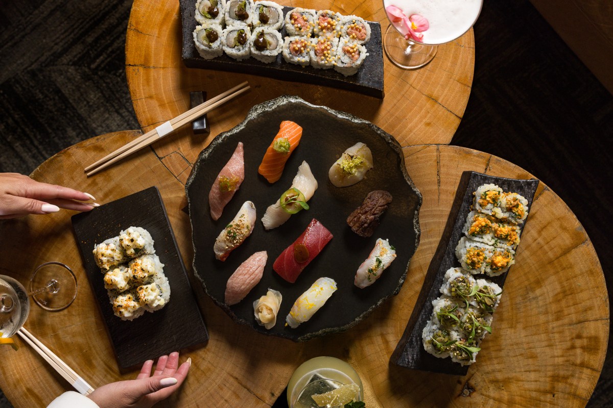 Overhead view of assorted sushi platters and rolls on a wood table with cocktails