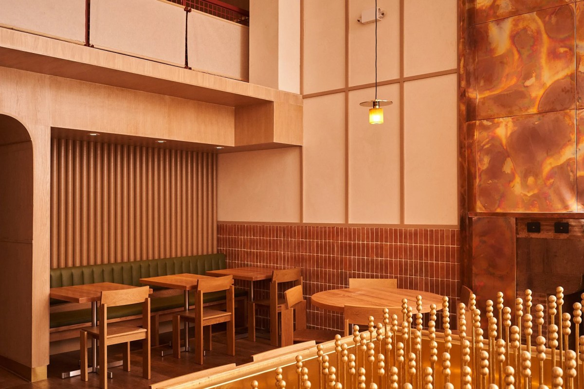 Warm-toned dining room with wood tables, green banquette seating, copper wall panel and brass railing details
