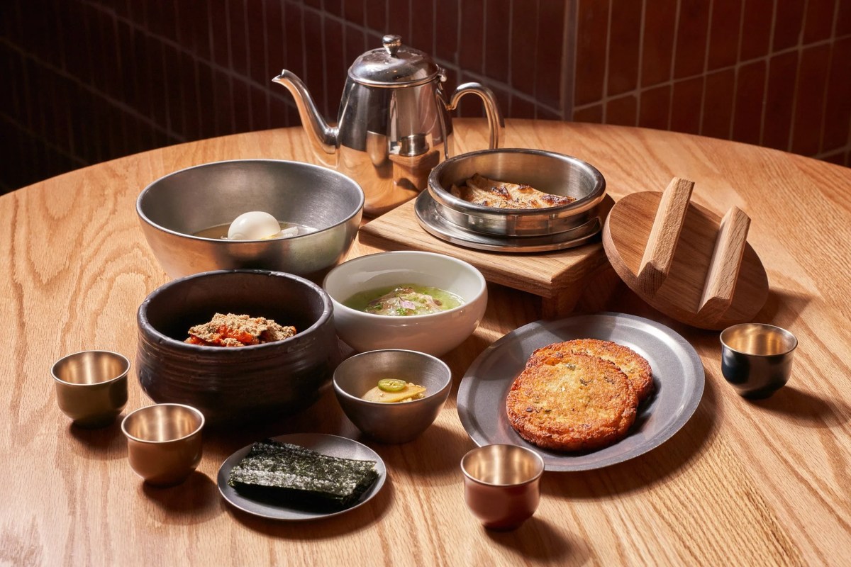 Round wooden table set with multiple Korean dishes, metal bowls, teapot, and small cups