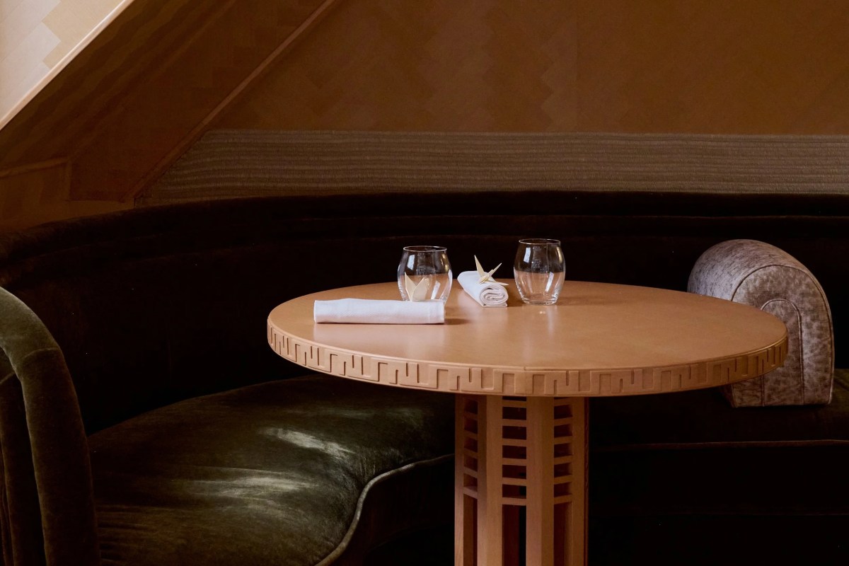 Close view of a round wood table with glasses and folded napkins against a velvet banquette