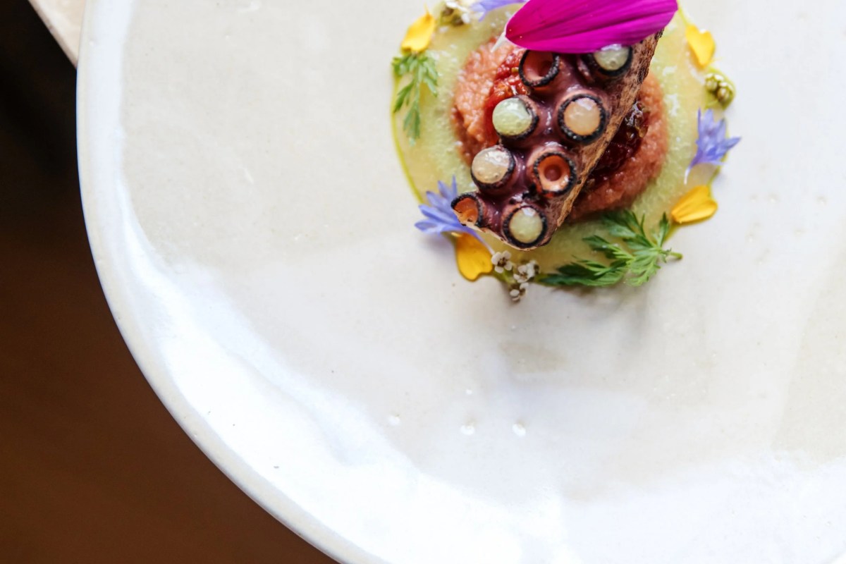 Plated dish with octopus, tomato, melon, and edible flowers on a white plate