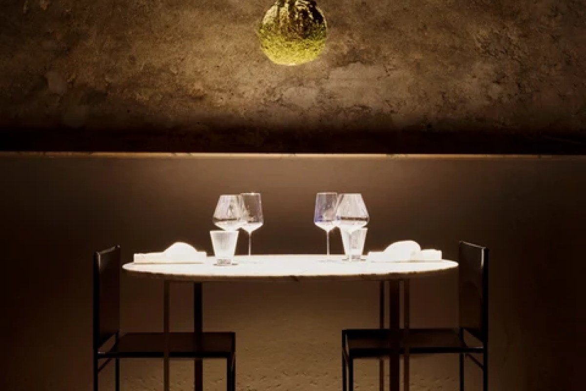 Candlelit dining table for two with wine glasses and folded napkins against a textured dark wall