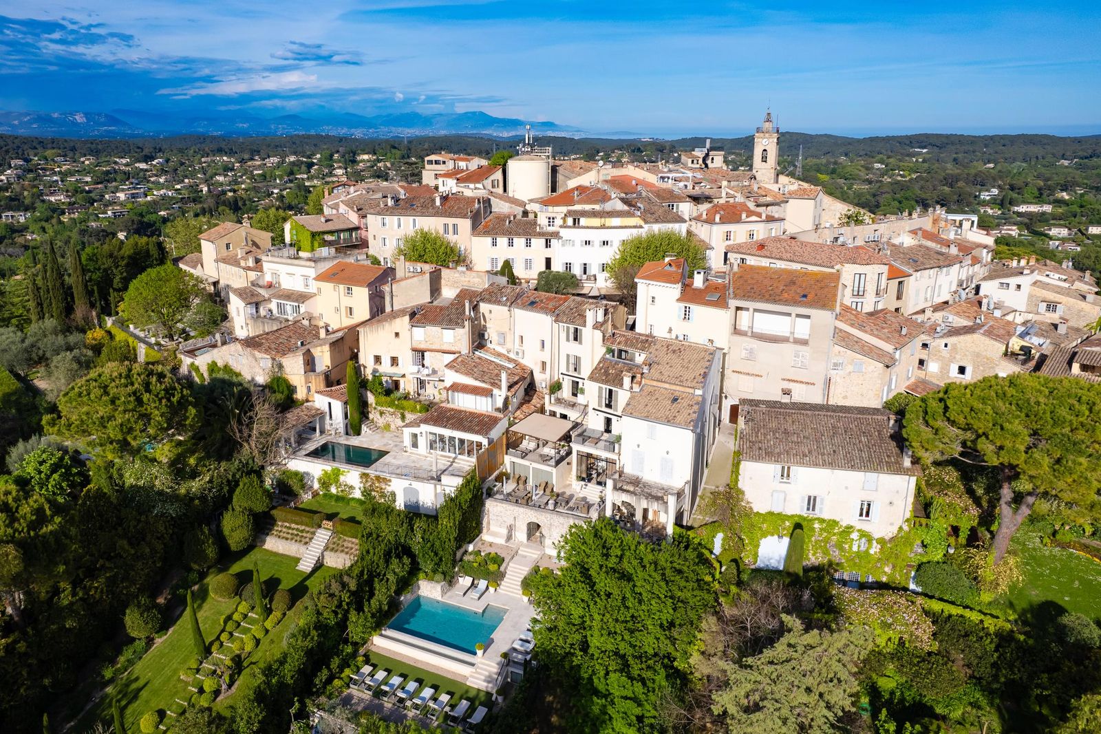 The hilltop village of Mougins from the air: the church tower, stone houses and terraced gardens ringed by pines, with the hills behind