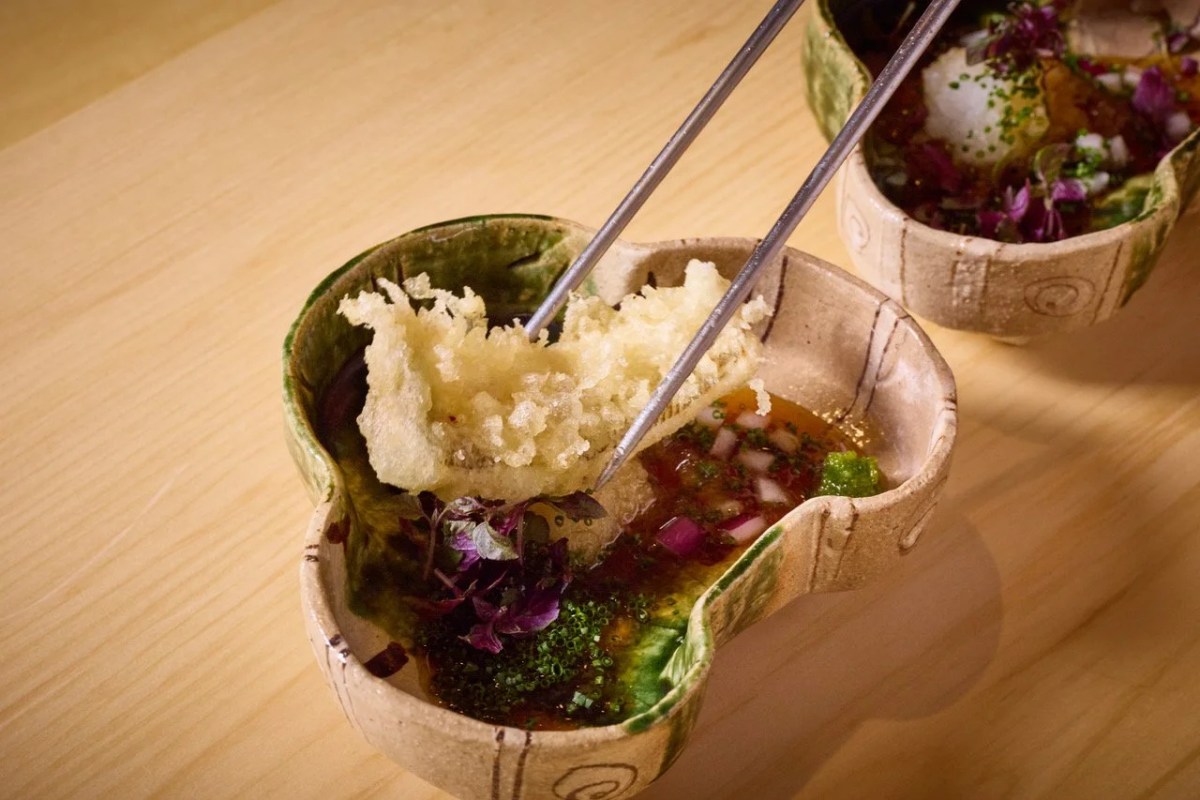 A dish with tempura, herbs and sauce in a ceramic bowl, chopsticks lifting food