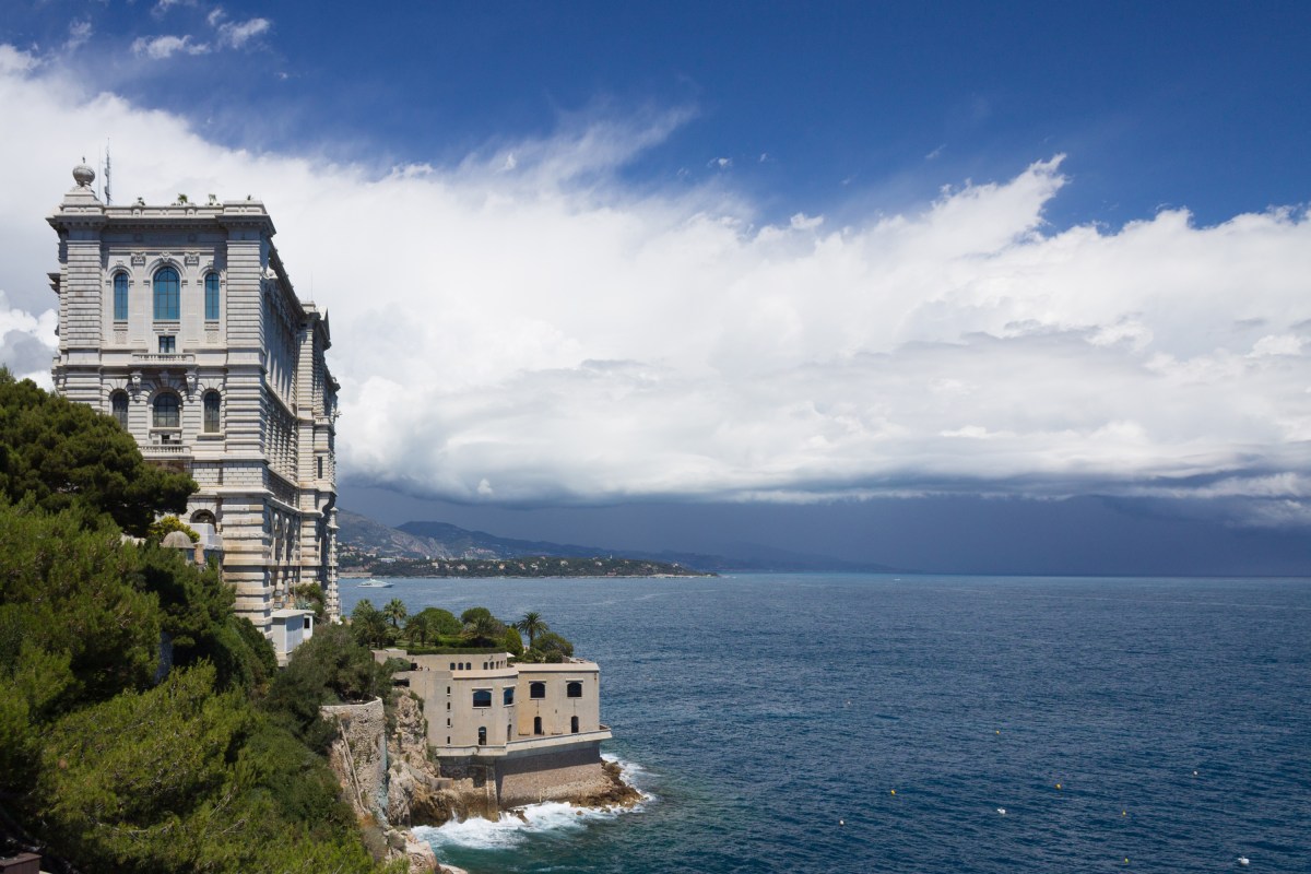 Oceanographic Museum's grand stone facade on a rocky cliff edge with dramatic sky and sea view.