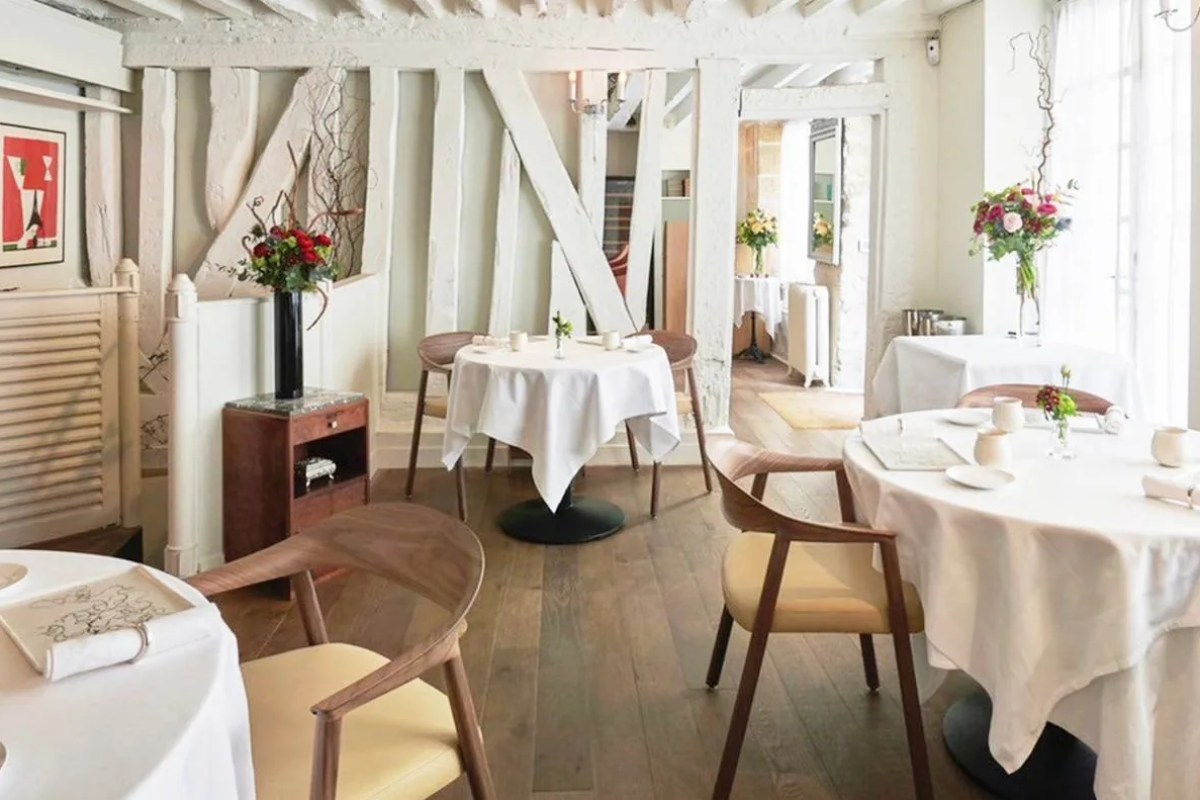 Elegant dining room with white-clothed round tables, wooden chairs, exposed whitewashed beams and fresh flowers
