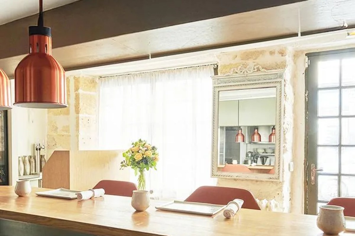 Restaurant counter area with copper pendant lights, stone wall, mirror reflecting kitchen, flowers on wooden bar
