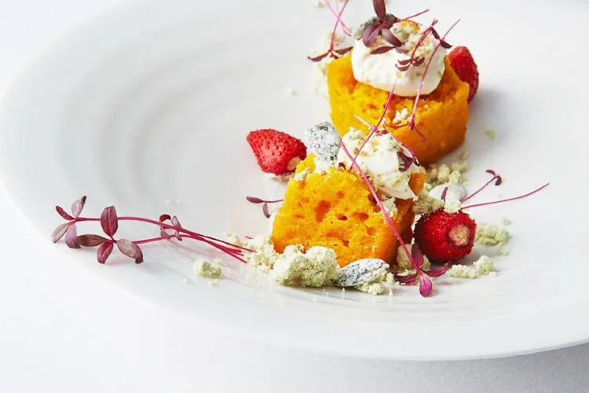 Close-up plated dessert: orange sponge cake, whipped cream, strawberries and herb garnish on white plate