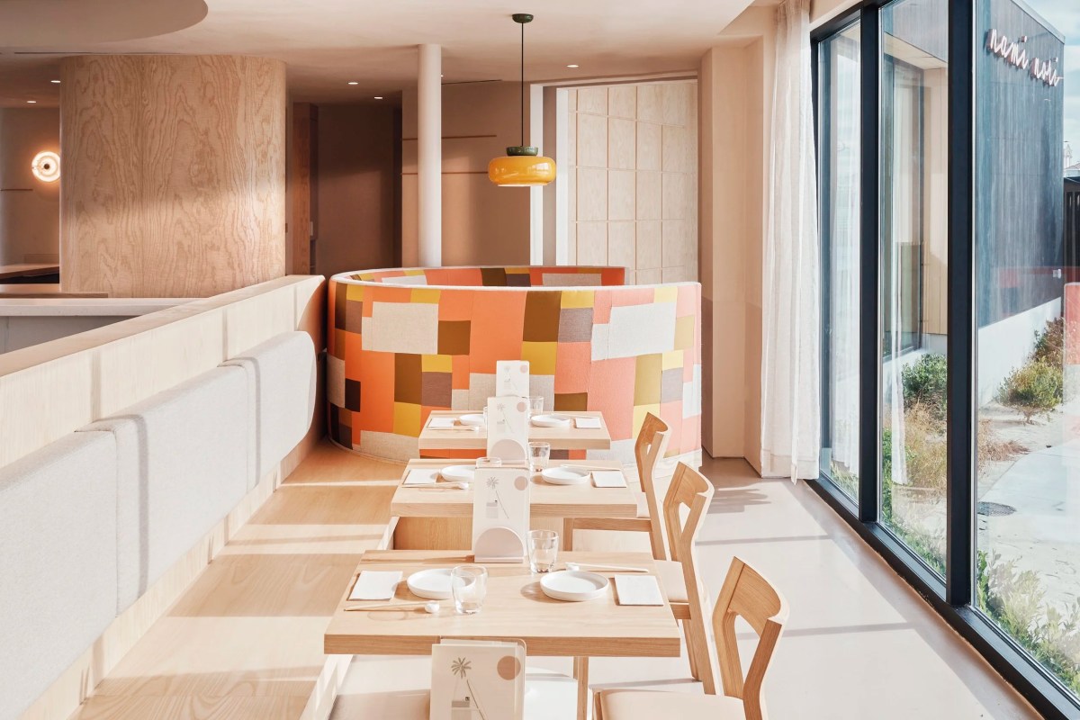 Bright dining room with colorful patchwork booth, wood tables, and glowing 'nami nori' sign visible through window
