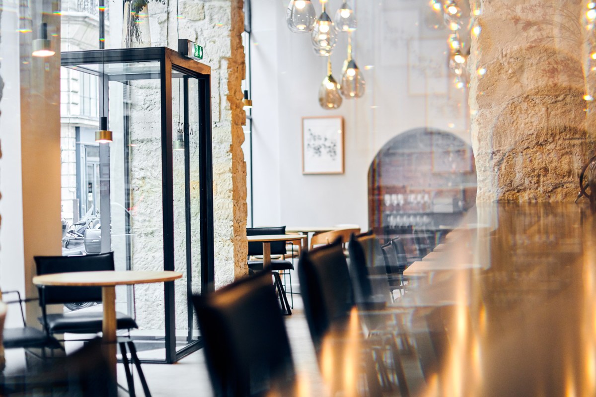 Interior dining room of NESO restaurant in Paris, with exposed stone walls, wooden tables, black chairs, and hanging glass pendant lights