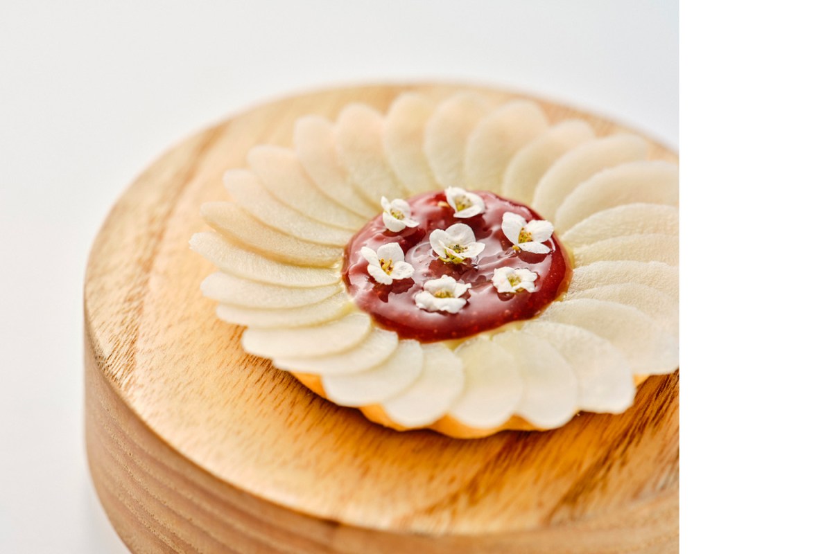 Delicate tart with thin pear slices, red fruit coulis, and small white flowers on a wooden board