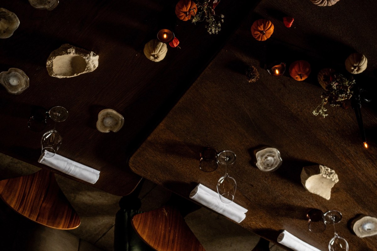 Overhead view of dark wooden restaurant tables set with wine glasses, rolled white napkins, candles and small pumpkins