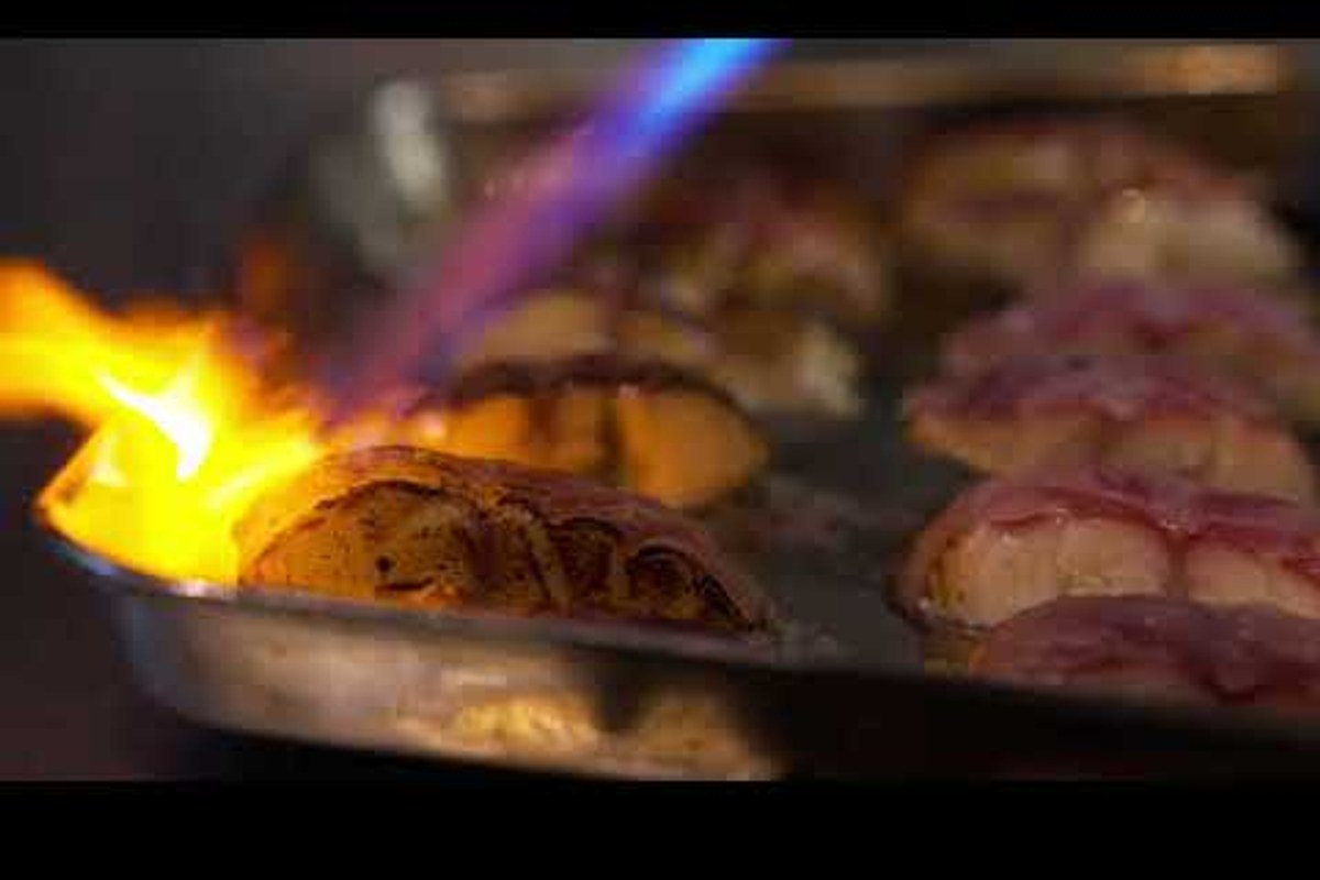 Close-up of scallops being seared with a blowtorch flame on a tray