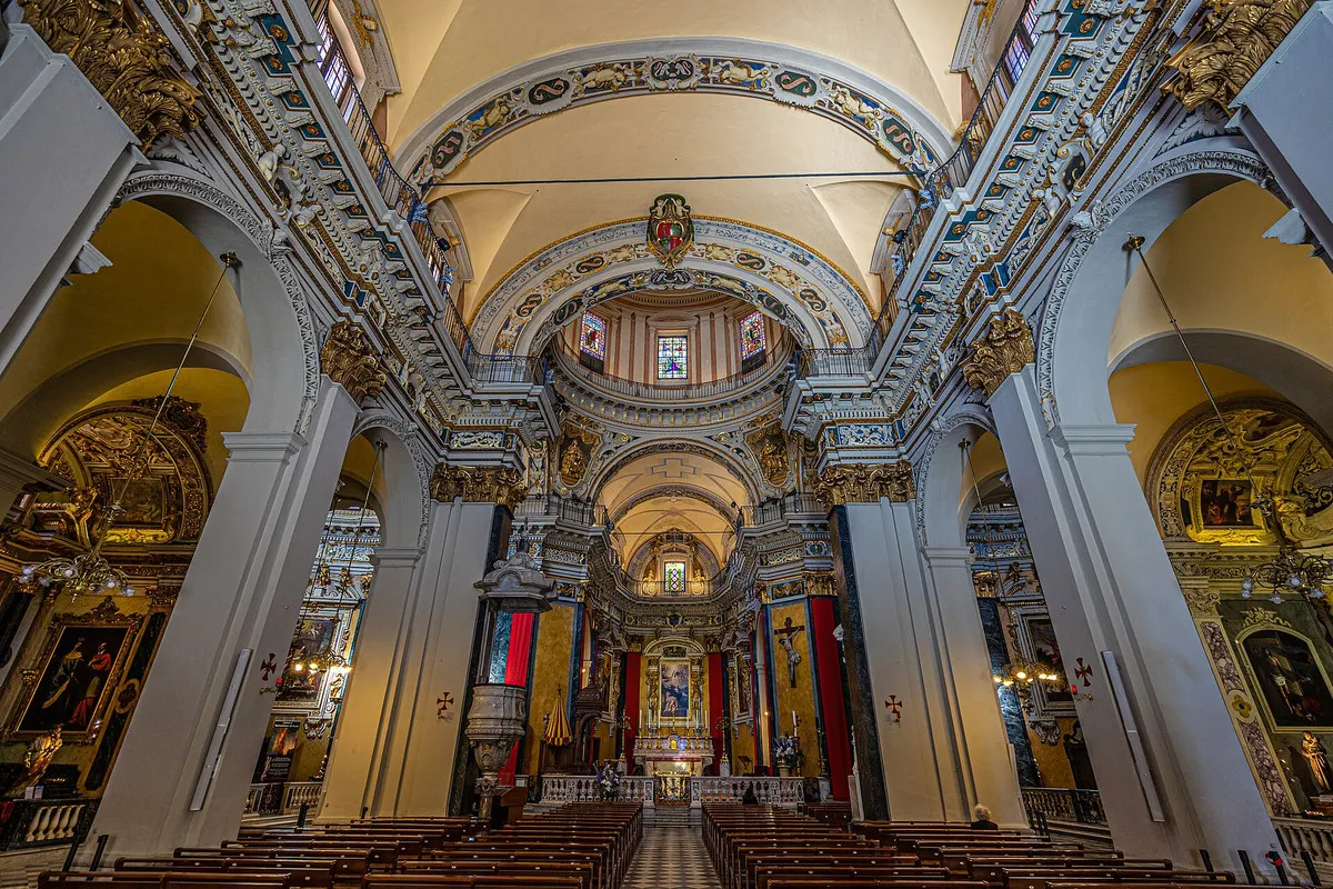 The baroque nave of the Cathédrale Sainte-Réparate in Nice, with white and gilded stucco, painted vaults and the high altar beneath the dome
