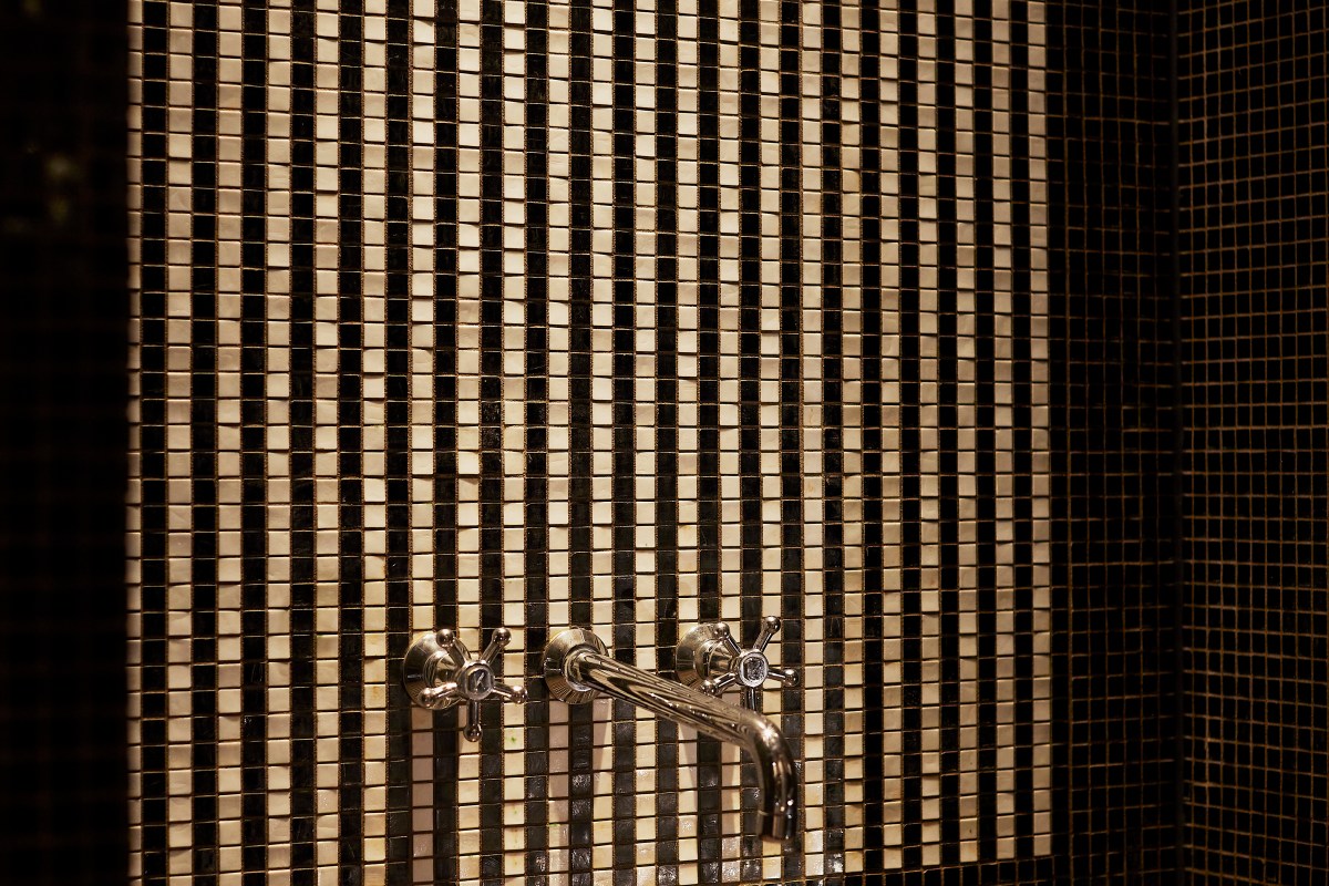 Detail of a mosaic-tiled shower wall with polished chrome fixtures, likely in a guest bathroom
