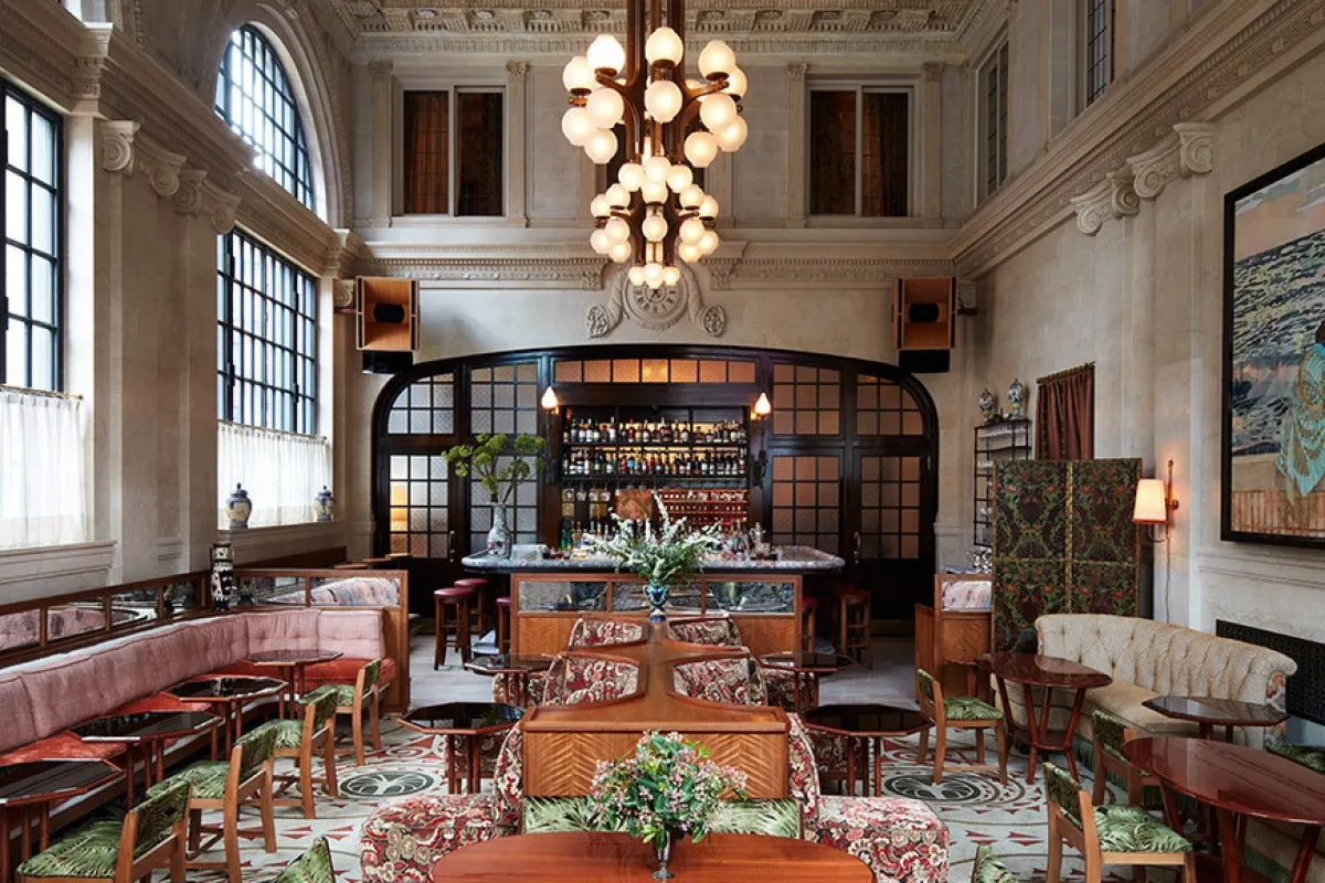 Grand bar and lounge with soaring ceilings, arched windows, and a large sculptural chandelier