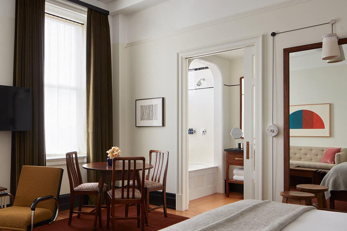 Guest room with bed, seating area, round table, and view into bathroom with tub and shower