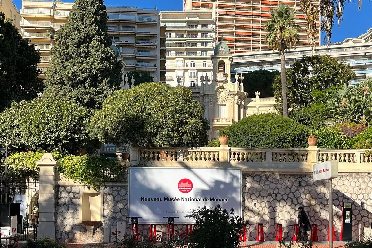 The entrance to Villa Sauber with the Nouveau Musée National de Monaco sign, the Belle Époque villa behind the garden, and high-rise buildings in Larvotto