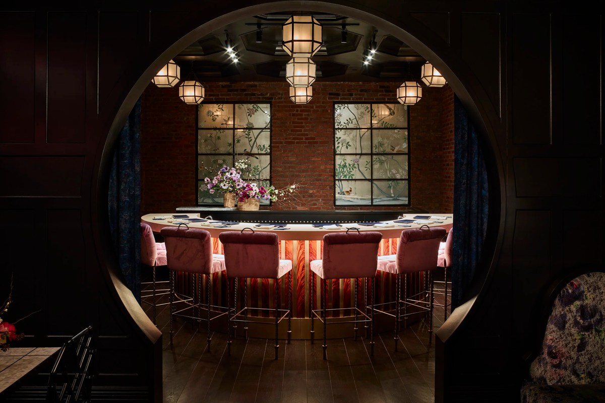 Elegant restaurant interior view through a round moon-gate archway showing a bar with pink velvet stools, pendant lanterns, and floral mural windows.