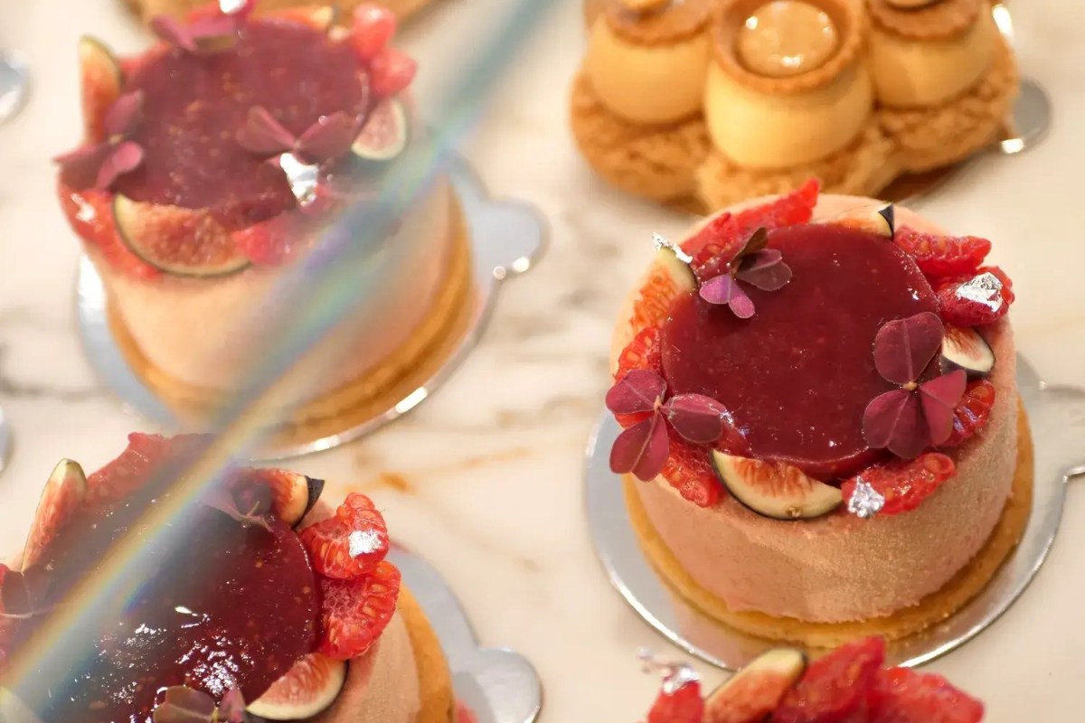 Overhead view of individual fruit tarts with fig, raspberry and edible flower garnish on marble counter