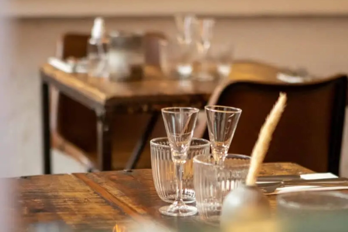 Close-up of a rustic wooden dining table with wine glasses and cutlery, blurred dining room in background