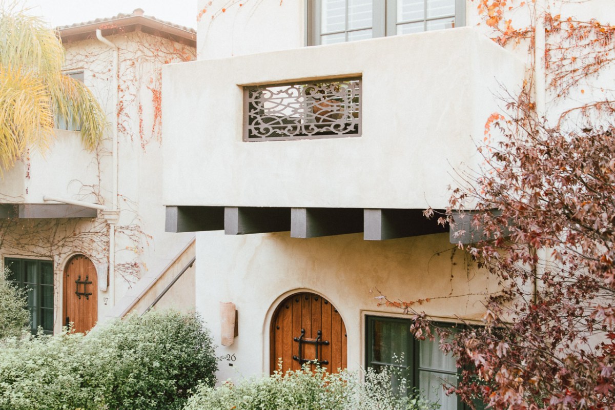 Exterior façade of North Block Hotel showing stucco walls, arched wooden door, balcony, and lush greenery.
