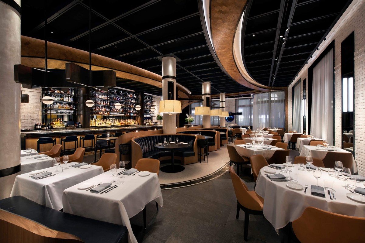 Modern restaurant dining room with white-clothed tables, curved booth seating, and a well-stocked bar under a sculptural ceiling