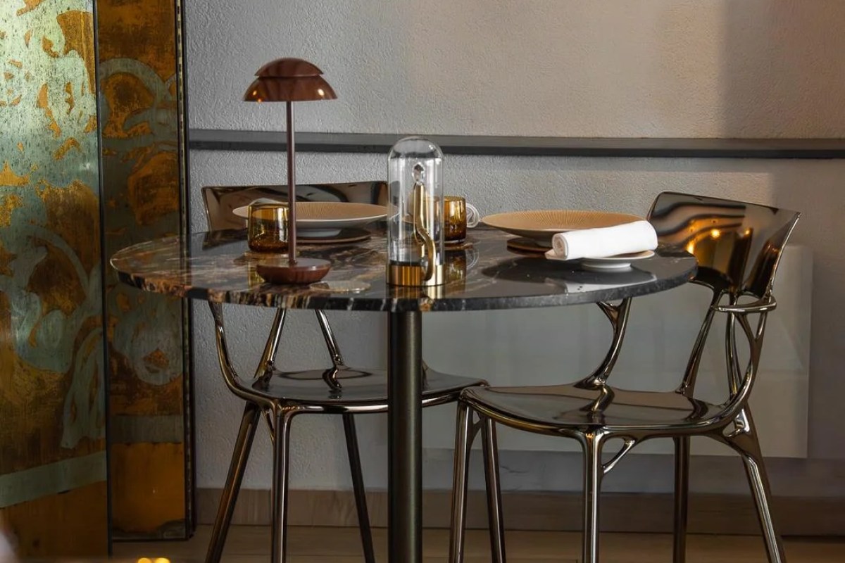 Elegant restaurant table set with plates, napkin, lamp, and decorative screen in background.