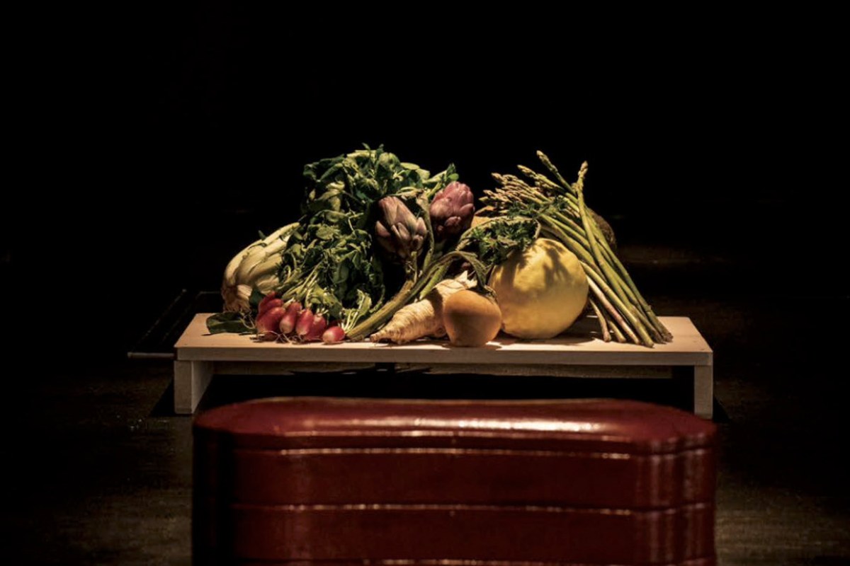 Fresh vegetables including asparagus, artichokes, and radishes displayed on a wooden table over a red lacquer box.