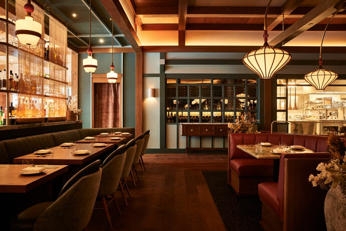 Wide view of dining room with wine display, open kitchen, bar, and red leather booths under pendant lights