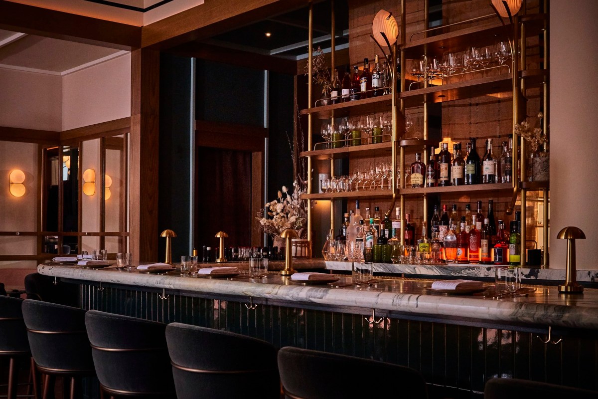 Marble-topped bar with shelves of liquor bottles and glassware, lit by pendant lamps