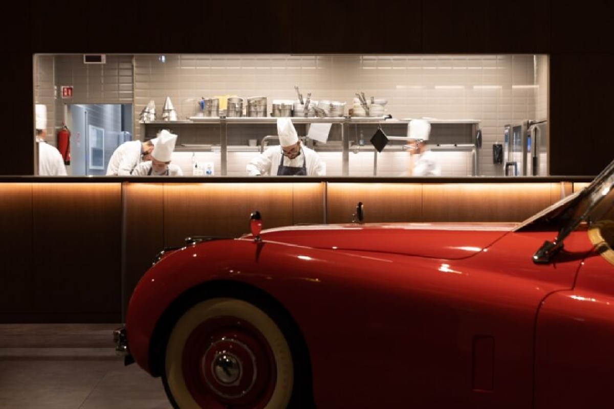 Vintage red car in foreground with open kitchen and chefs visible behind counter