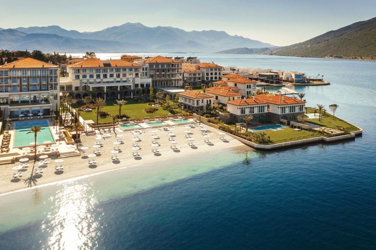 Aerial view of One&Only Portonovi hotel complex with pools, beach and terracotta rooftops by the sea, mountains behind