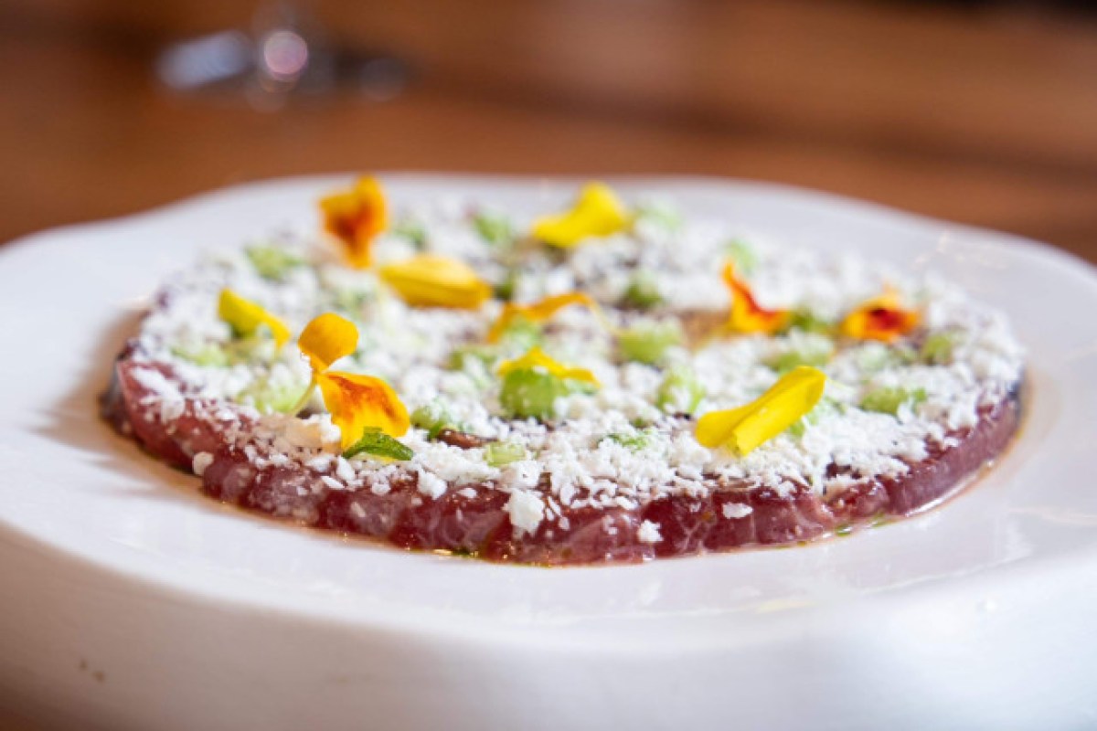 Thinly sliced beef carpaccio topped with grated cheese and edible flowers on a white plate