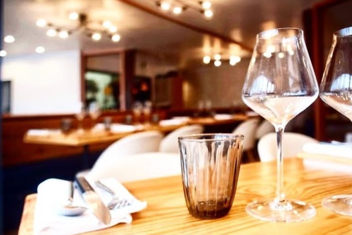 Restaurant dining room interior with wooden tables, white chairs and wine glasses in foreground