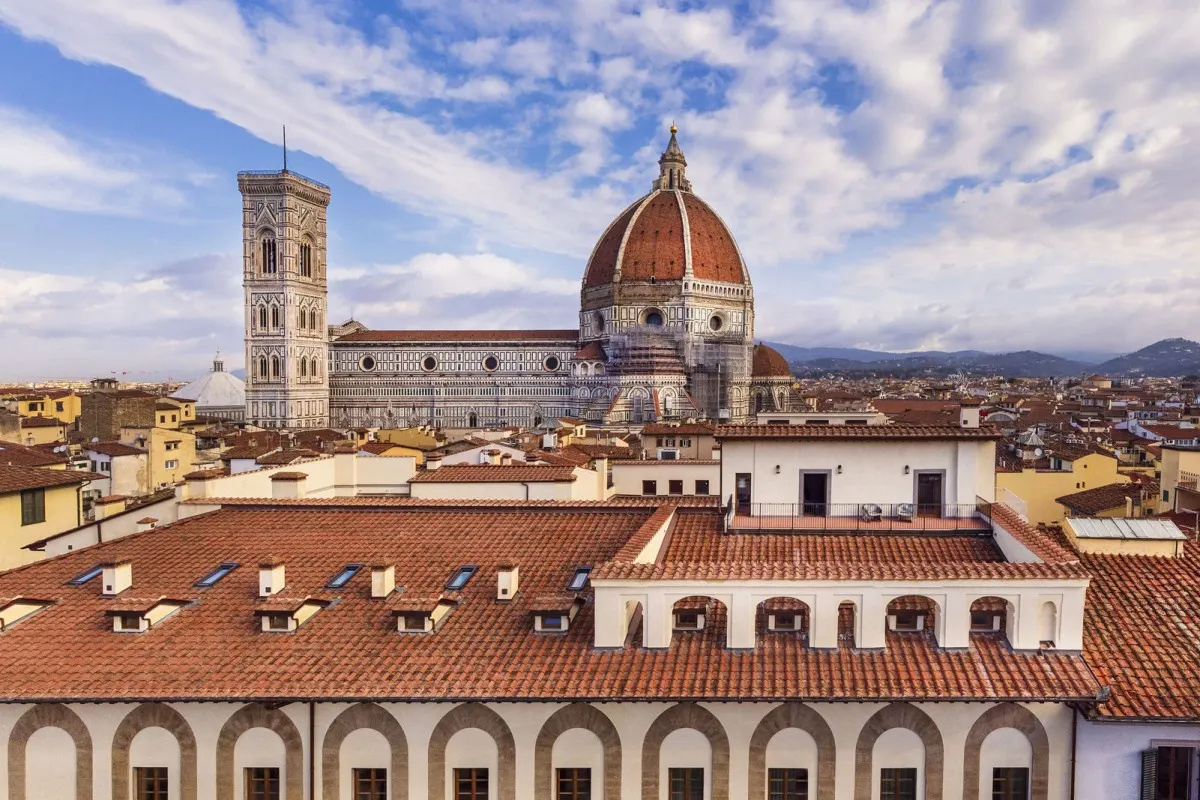 The tiled roofs and arched top floor of Palazzo Portinari Salviati in Florence, with the Duomo's dome and Giotto's bell tower behind