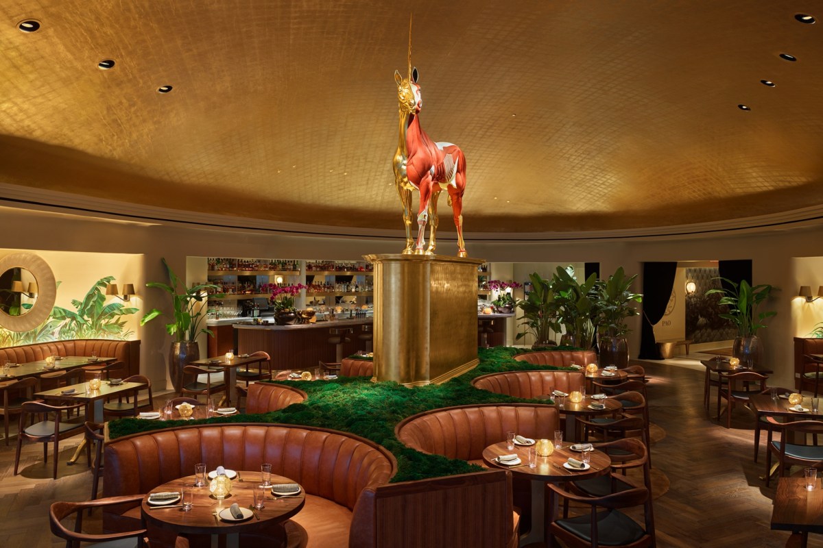 Pao by Paul Qui dining room with curved leather banquettes, moss landing strip, and gold anatomical unicorn statue