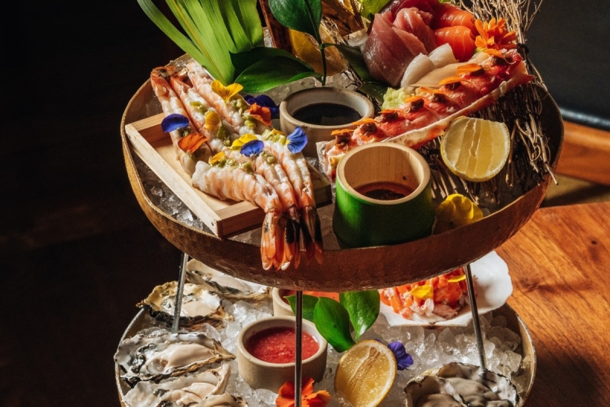 Tiered seafood platter with shrimp, sashimi, oysters, citrus, and dipping sauces on ice