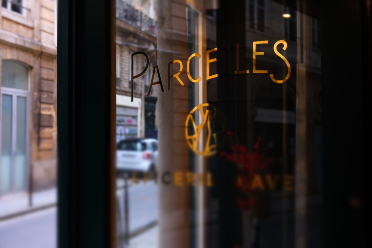 Gold "Parcelles" lettering on the restaurant's glass storefront window, with Paris street reflected in the glass.
