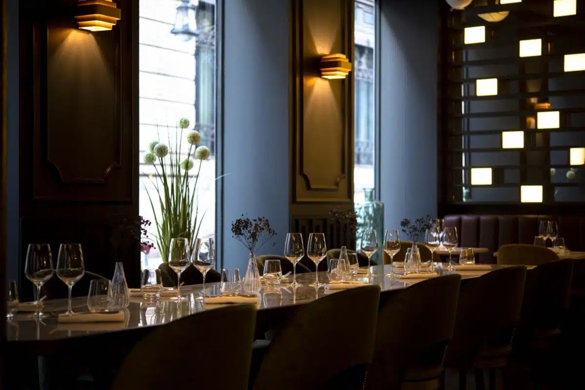 Elegant dark wood dining room with long marble table, wine glasses, and art deco wall lighting