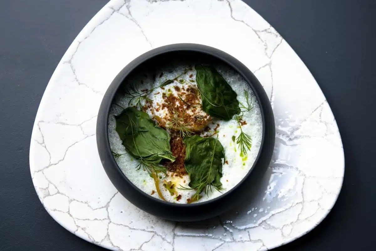 Artfully plated dish with greens, herbs, and a creamy sauce on a triangular marble-patterned plate