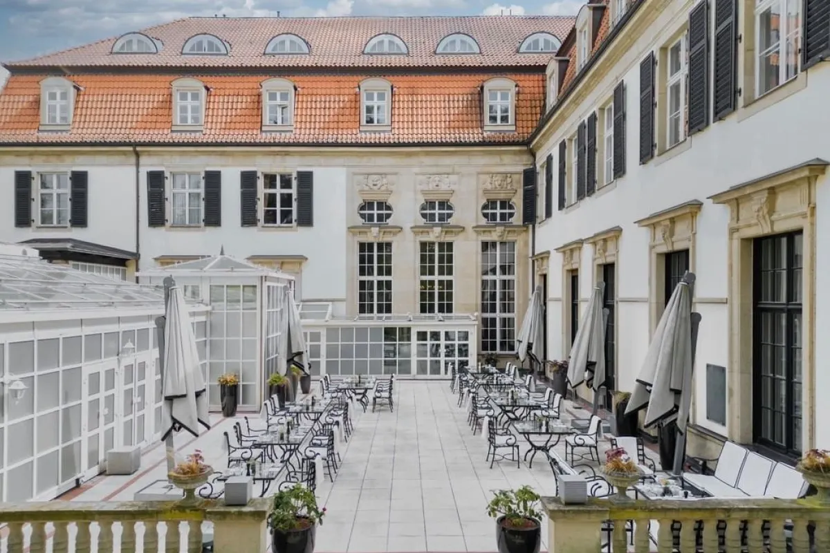 Interior courtyard terrace with outdoor dining tables, chairs, and umbrellas, framed by the hotel's historic facade and glass conservatory.