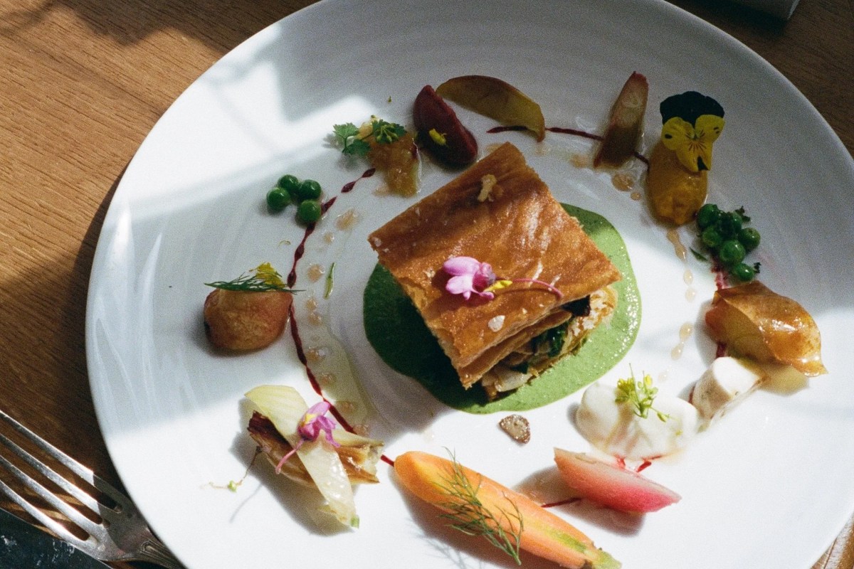 Overhead shot of an elegant plated dish with pastry, peas, edible flowers and colorful garnishes on a white plate.