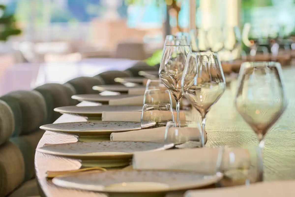 Close-up of a long dining table set with wine glasses and plates, terrace ambiance