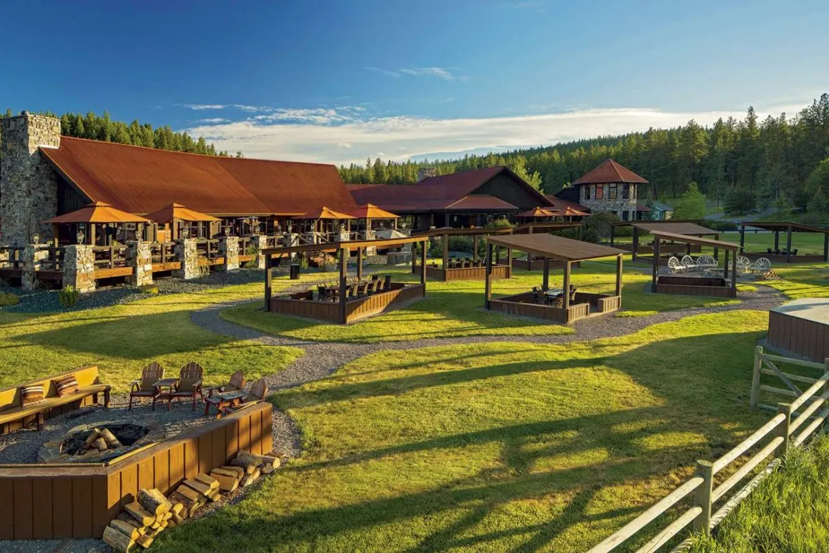 Main lodge building exterior with red roof, stone chimneys, covered walkways and fire pit lawn area at sunset