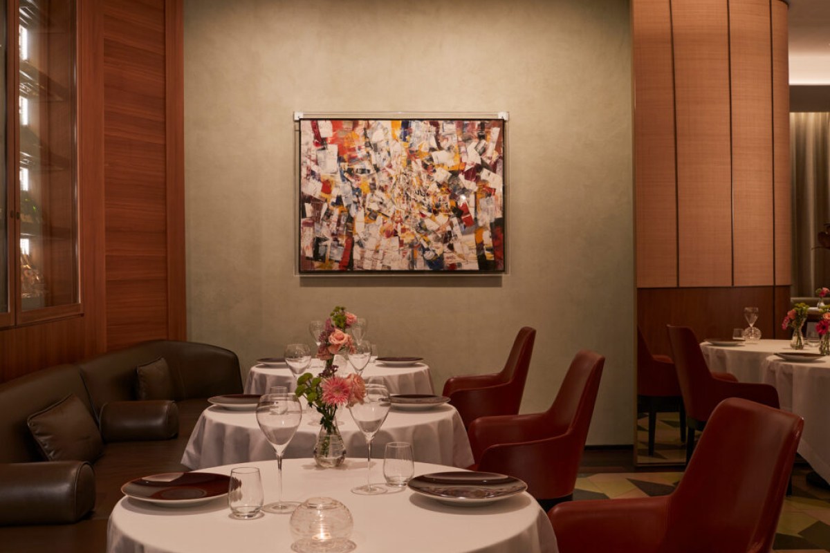 Elegant dining room with round tables, white linens, red leather chairs, and abstract art