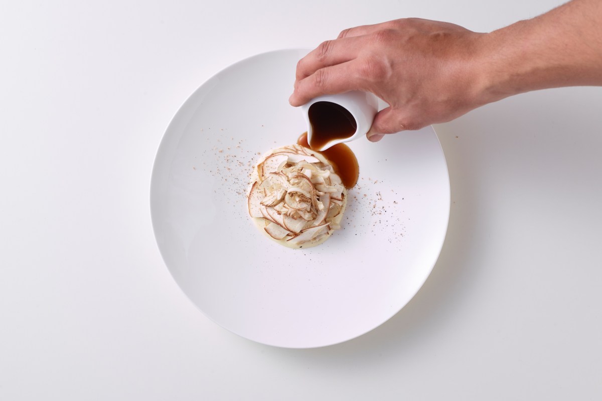Sauce being poured beside a porcino mushroom dish on a white plate
