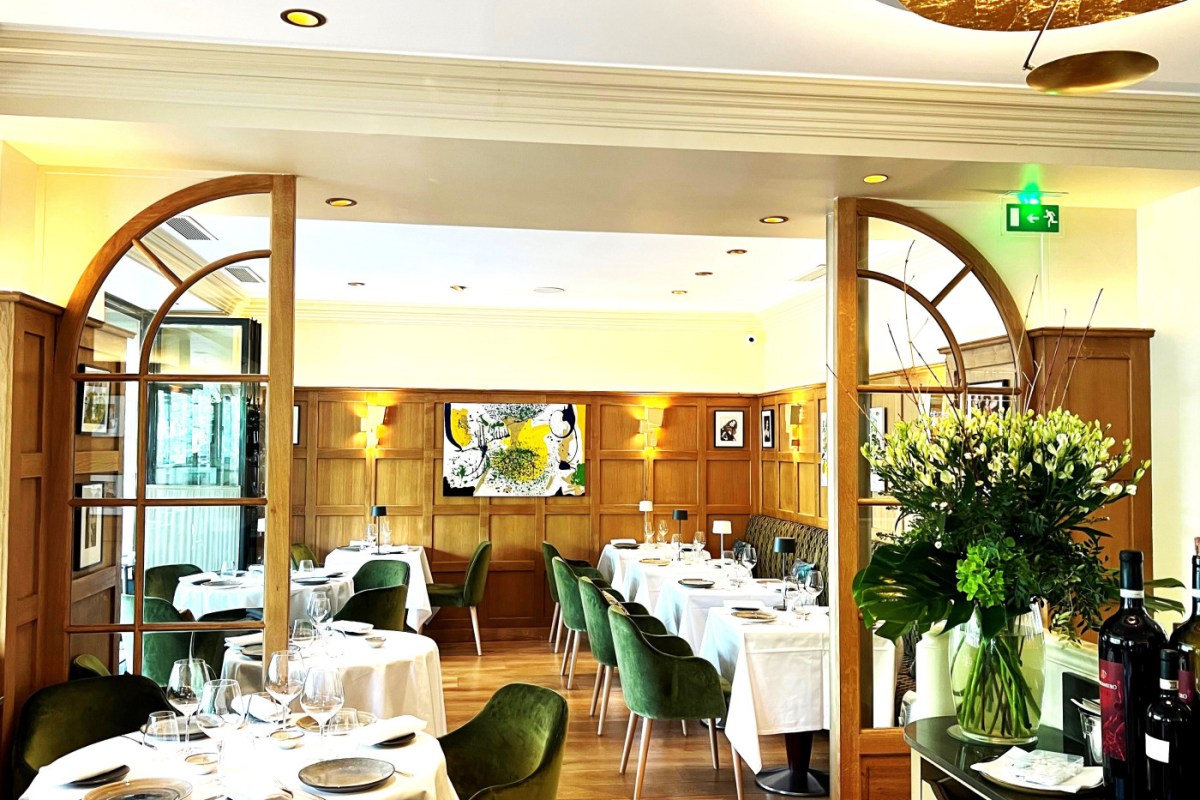 Elegant dining room with white-clothed tables, green velvet chairs, wood paneling, and a large floral arrangement.